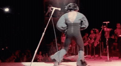 A Man Is Singing Into A Microphone On A Stage . GIF