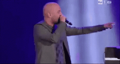 A Man Is Singing Into A Microphone On A Stage And Pointing At Something . GIF