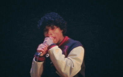A Man Is Singing Into A Microphone On A Stage In Front Of A Crowd . GIF