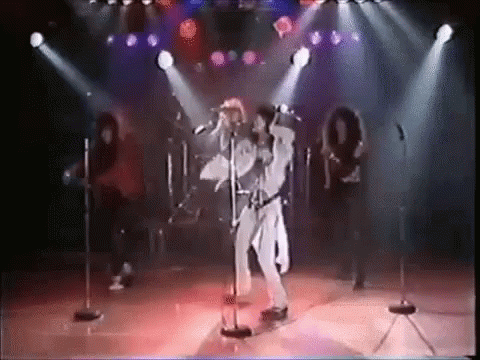 A Man Is Singing Into A Microphone On A Stage In Front Of A Group Of People . GIF