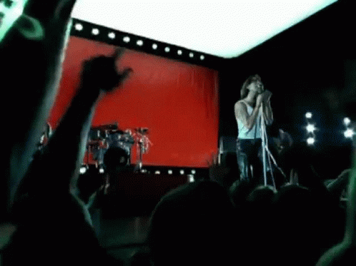 A Man Is Singing Into A Microphone On A Stage In Front Of A Red Curtain . GIF