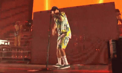 A Man Is Singing Into A Microphone On A Stage In Front Of A Red Wall . GIF