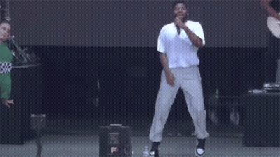 A Man Is Singing Into A Microphone On A Stage While Dancing . GIF