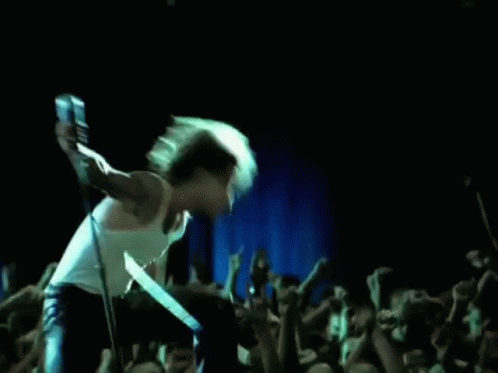 A Man Is Singing Into A Microphone On Stage In Front Of A Crowd . GIF