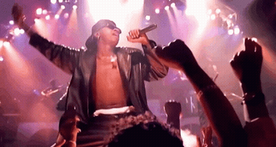 A Man Is Singing Into A Microphone On Stage In Front Of A Crowd Of People . GIF