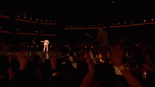 A Man Is Singing Into A Microphone While Another Man Plays A Guitar Behind Him . GIF