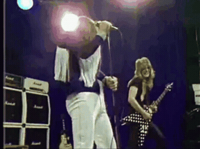 A Man Is Singing Into A Microphone While Another Man Plays A Guitar On Stage . GIF