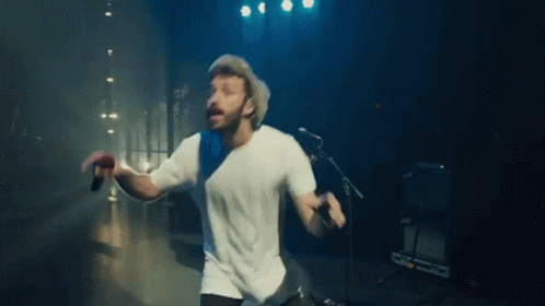 A Man Is Singing Into A Microphone While Dancing On A Stage . GIF
