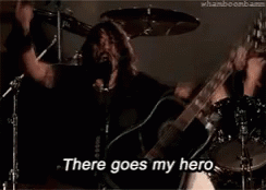 A Man Is Singing Into A Microphone While Holding A Guitar And Saying There Goes My Hero GIF