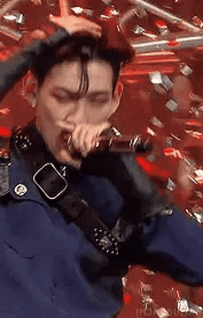 A Man Is Singing Into A Microphone While Holding His Hair . GIF