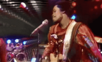 A Man Is Singing Into A Microphone While Playing A Guitar . GIF