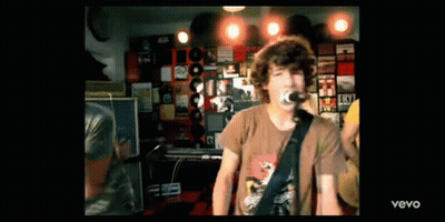 A Man Is Singing Into A Microphone While Playing A Guitar In A Room With Records On The Wall . GIF