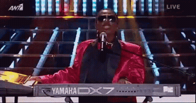 A Man Is Singing Into A Microphone While Playing A Yamaha Dx7 Keyboard . GIF