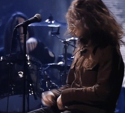 A Man Is Singing Into A Microphone While Playing Drums GIF