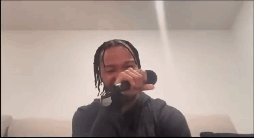 A Man Is Singing Into A Microphone While Sitting On A Couch In A Room . GIF