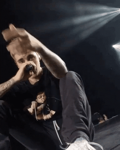 A Man Is Singing Into A Microphone While Sitting On A Stage GIF