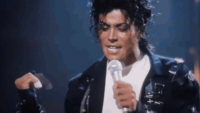 A Man Is Singing Into A Microphone While Wearing A Black Jacket GIF