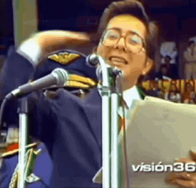 A Man Is Singing Into A Microphone While Wearing A Military Hat And Glasses . GIF