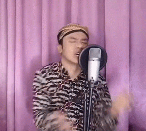 A Man Is Singing Into A Microphone While Wearing A Turban . GIF