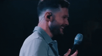 A Man Is Singing Into A Microphone While Wearing Earbuds . GIF