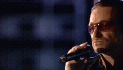 A Man Is Singing Into A Microphone While Wearing Sunglasses . GIF