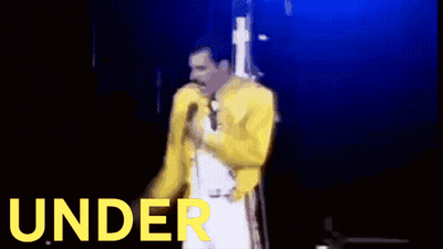 A Man Is Singing Into A Microphone With A Drum Set In The Background GIF