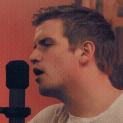 A Man Is Singing Into A Microphone With A Red Background GIF