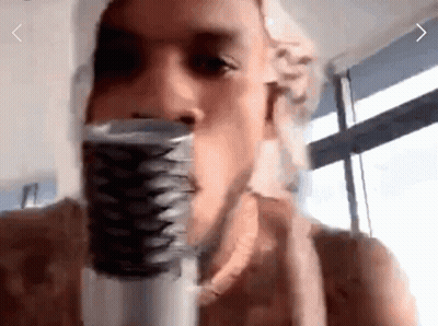 A Man Is Singing Into A Microphone With A Window Behind Him GIF