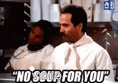 A Man Is Sitting At A Counter In A Kitchen Talking On A Cell Phone While Another Man Looks On . GIF