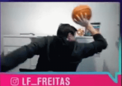 A Man Is Sitting At A Desk Holding A Basketball In His Hand . GIF