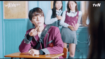 A Man Is Sitting At A Desk In A Classroom With Two Girls Standing Behind Him And A Tvn Logo In The Corner GIF