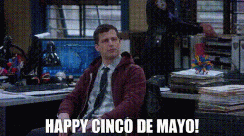 A Man Is Sitting At A Desk In An Office With The Words `` Happy Cinco De Mayo '' Written On The Screen . GIF