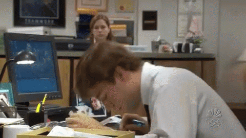 A Man Is Sitting At A Desk In Front Of A Computer And Eating A Sandwich . GIF