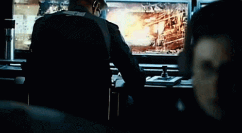 A Man Is Sitting At A Desk In Front Of A Computer Monitor With A Fire In The Background GIF