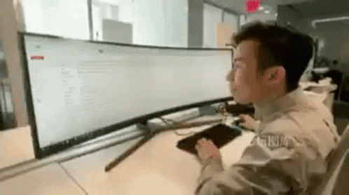 A Man Is Sitting At A Desk Looking At A Computer Monitor . GIF