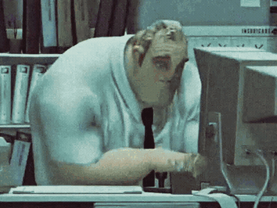 A Man Is Sitting At A Desk Looking At A Computer Monitor . GIF