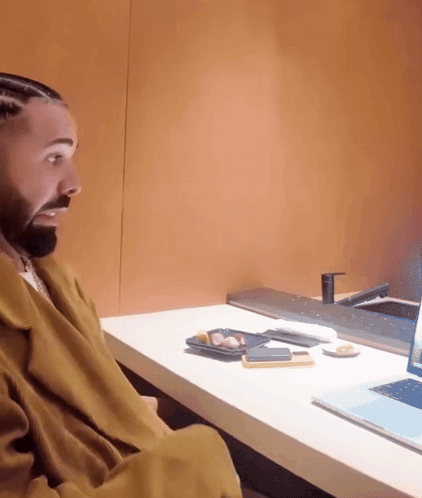 A Man Is Sitting At A Desk Looking At A Laptop Screen GIF