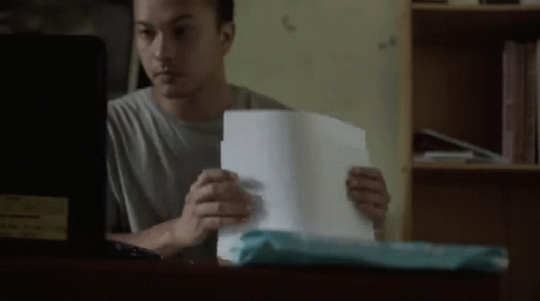 A Man Is Sitting At A Desk Looking At A Piece Of Paper . GIF