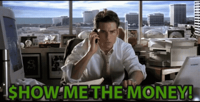 A Man Is Sitting At A Desk Talking On A Cell Phone With The Words Show Me The Money Written Below Him GIF