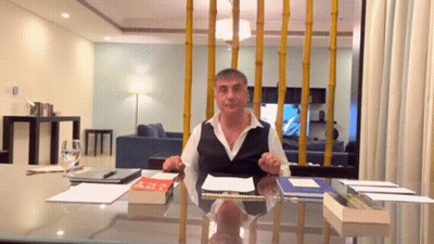 A Man Is Sitting At A Desk With A Book On It And A Glass Of Water In Front Of Him GIF