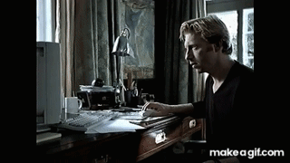 A Man Is Sitting At A Desk With A Computer And A Lamp On It . GIF