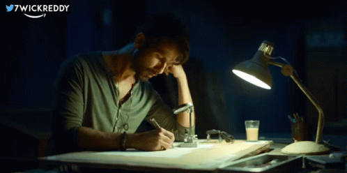 A Man Is Sitting At A Desk With A Lamp And Writing On A Piece Of Paper With 7Wickreddy Written In The Corner GIF