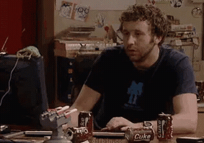A Man Is Sitting At A Desk With Cans Of Coke On It GIF