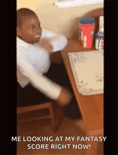 A Man Is Sitting At A Desk With His Arms Outstretched And Looking At His Fantasy Score Right Now . GIF