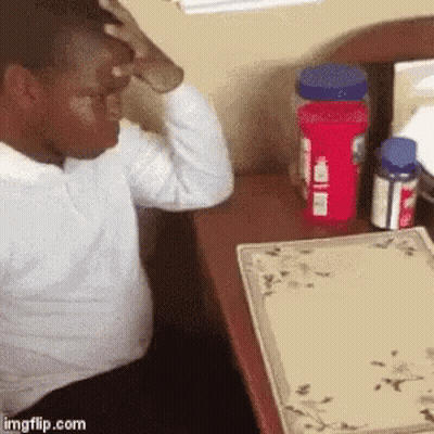 A Man Is Sitting At A Desk With His Hand On His Head And Bottles Of Medicine On The Table . GIF
