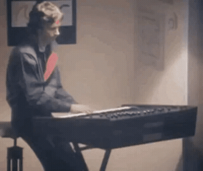 A Man Is Sitting At A Piano In A Room . GIF
