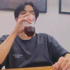 A Man Is Sitting At A Table Drinking A Glass Of Coffee . GIF