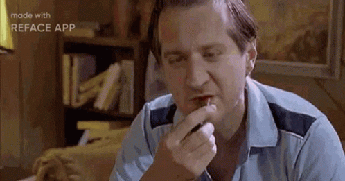 A Man Is Sitting At A Table Eating A Piece Of Food With His Mouth Open . GIF