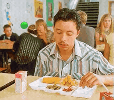 A Man Is Sitting At A Table Eating A Tray Of Food In A Cafeteria . GIF