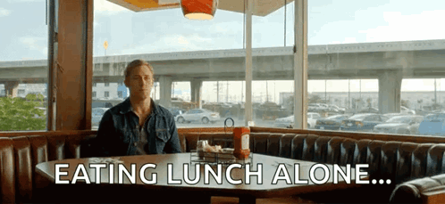 A Man Is Sitting At A Table Eating Lunch Alone GIF